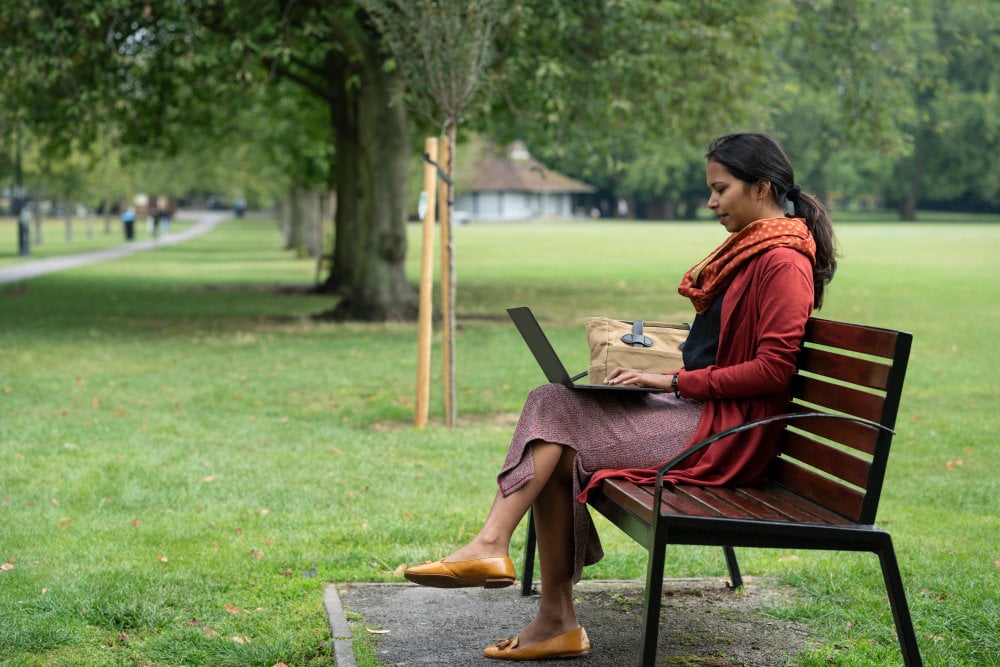 woman in India sitting on a bench taking a 5G course on her laptop